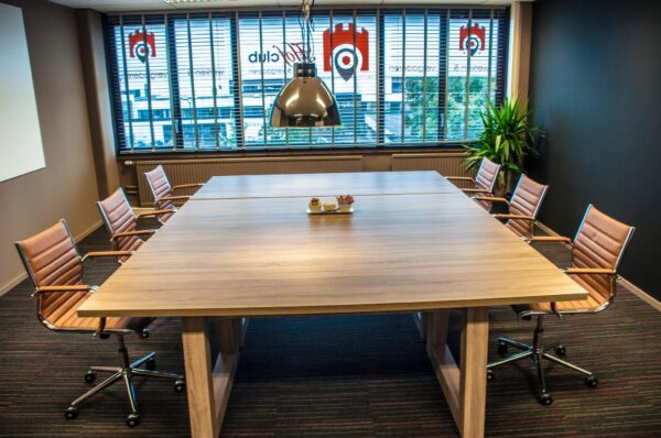 Vergaderruimte met houten tafel, zes bruine bureaustoelen en een grote hanglamp aan de Zaagmolenlaan.