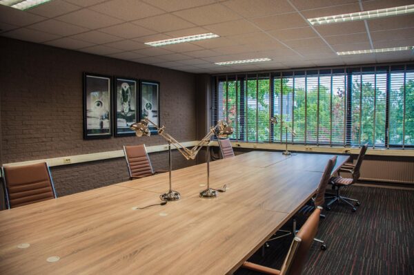 Vergaderruimte aan de Zaagmolenlaan met lange houten tafel, moderne bureaulampen, leren stoelen en grote ramen met uitzicht op groen.