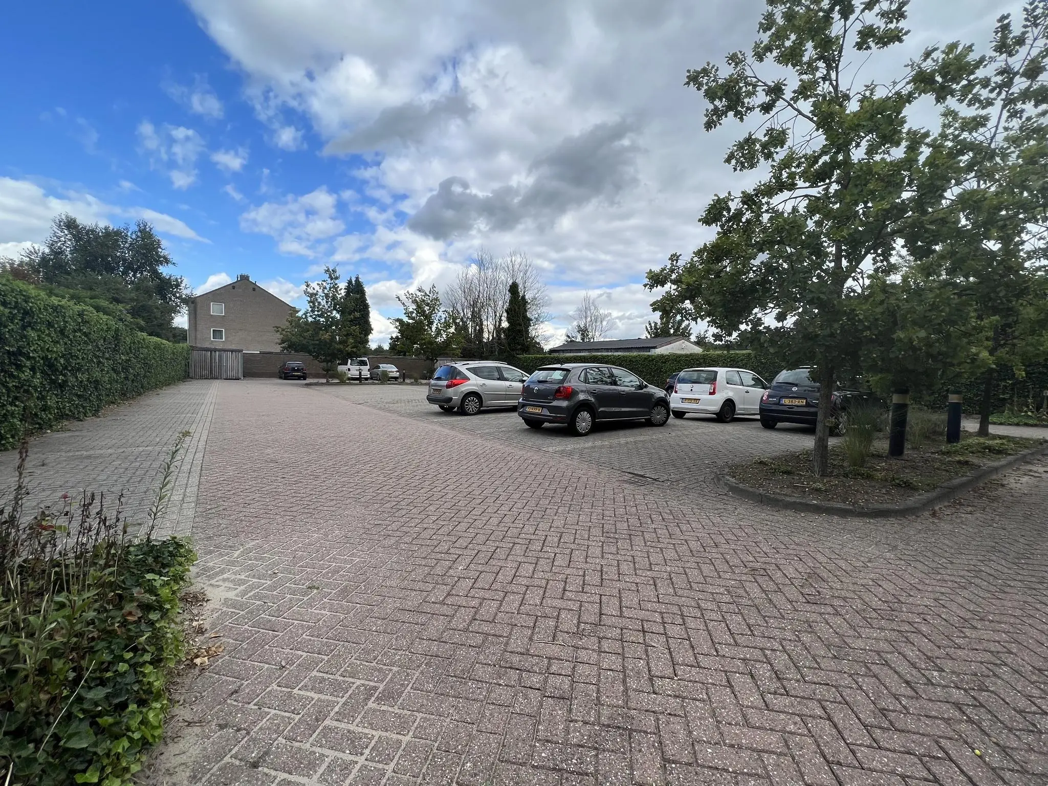 Parkeerplaats aan de Groenekanseweg met geparkeerde auto's, een woonhuis en bomen onder een deels bewolkte lucht.