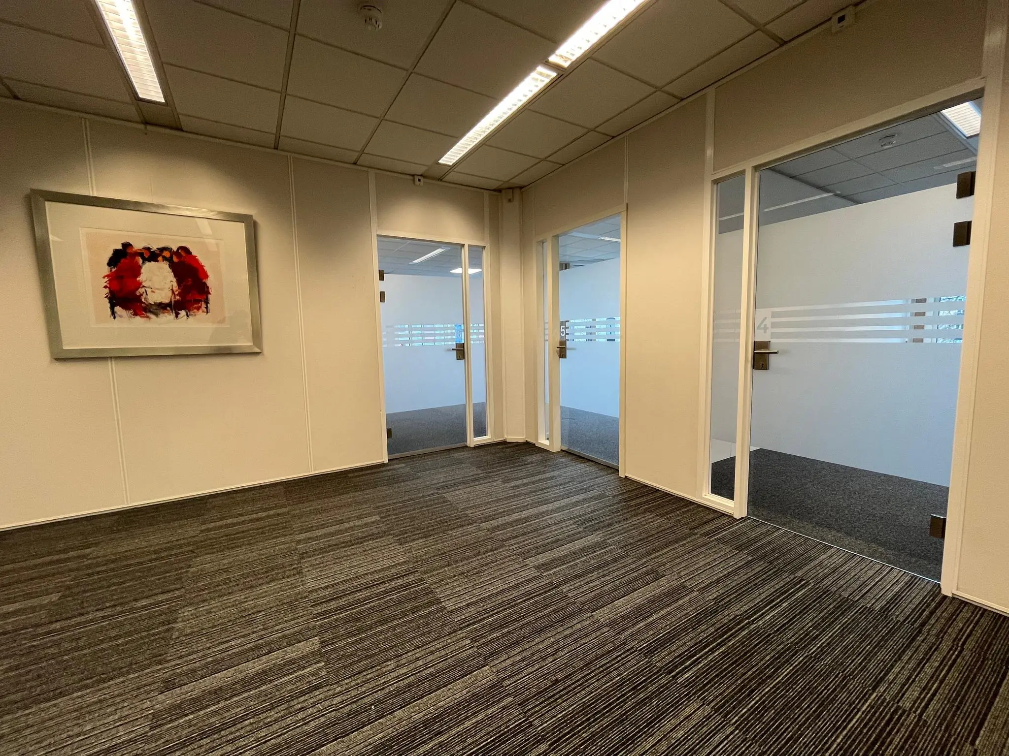 Kantoorruimte met tapijtvloer, glazen kantoordeuren en een abstract schilderij aan de muur aan de Utrechtseweg.