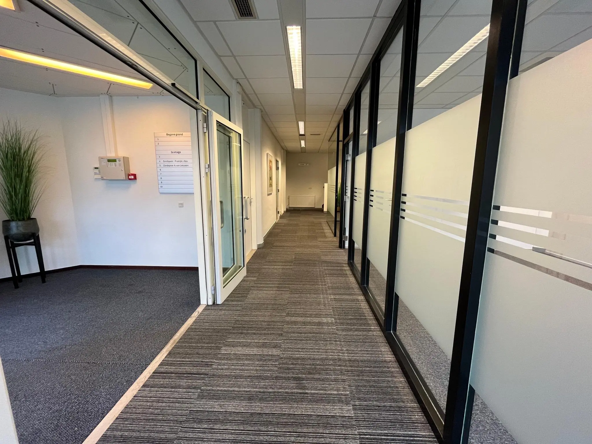 Gang in een kantoorpand aan de Utrechtseweg met glazen wanden en een overzichtsbord van bedrijven aan de muur.