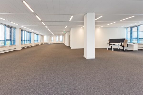 Ruime, moderne kantoorruimte in Kosterijland met tapijtvloer, systeemplafond en grote ramen met jaloezieën.