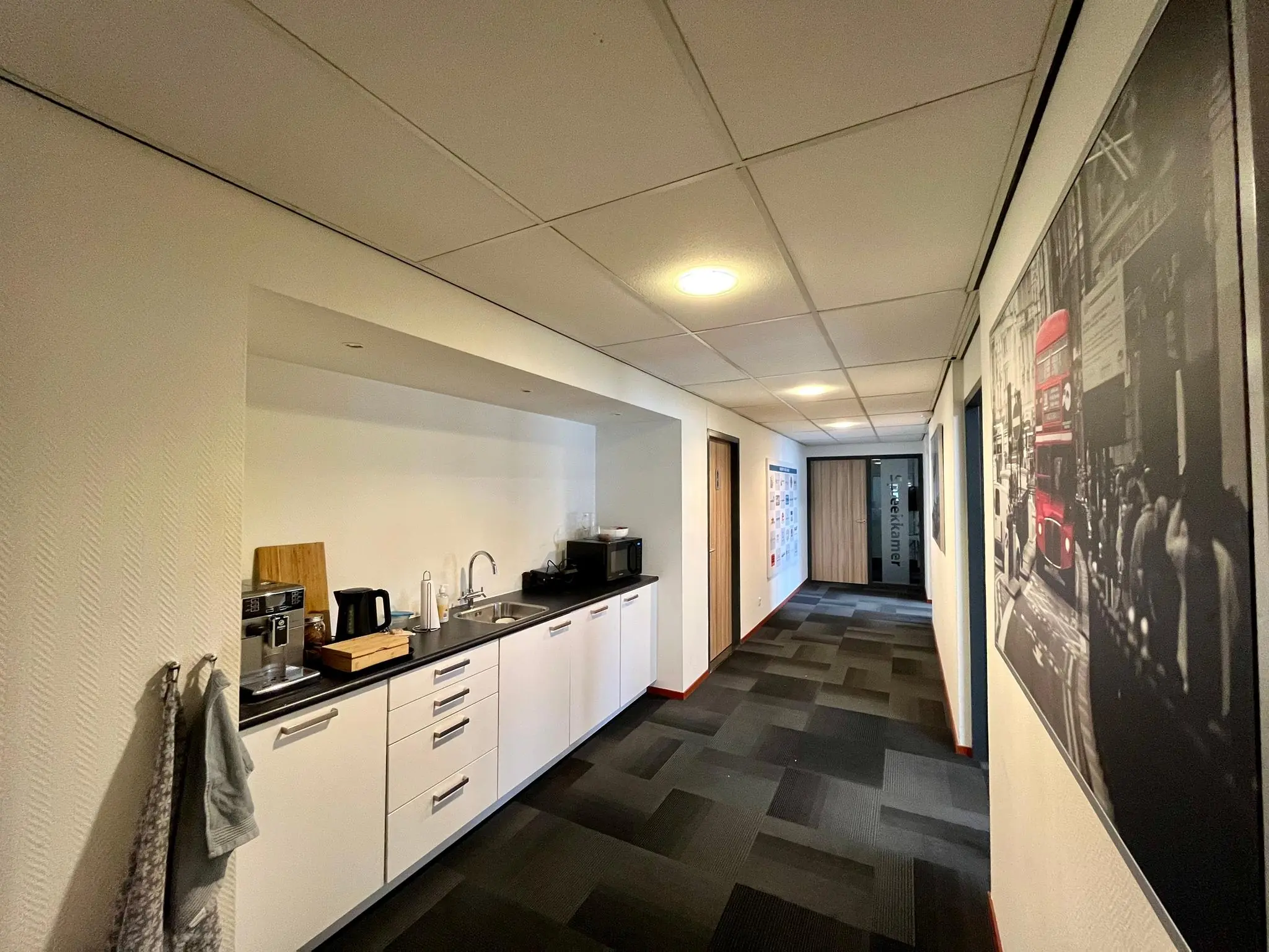 Een moderne kantoorhal aan de Daltonstraat met een kitchenette, koffieapparaat en een wandfoto van een Londense straat.