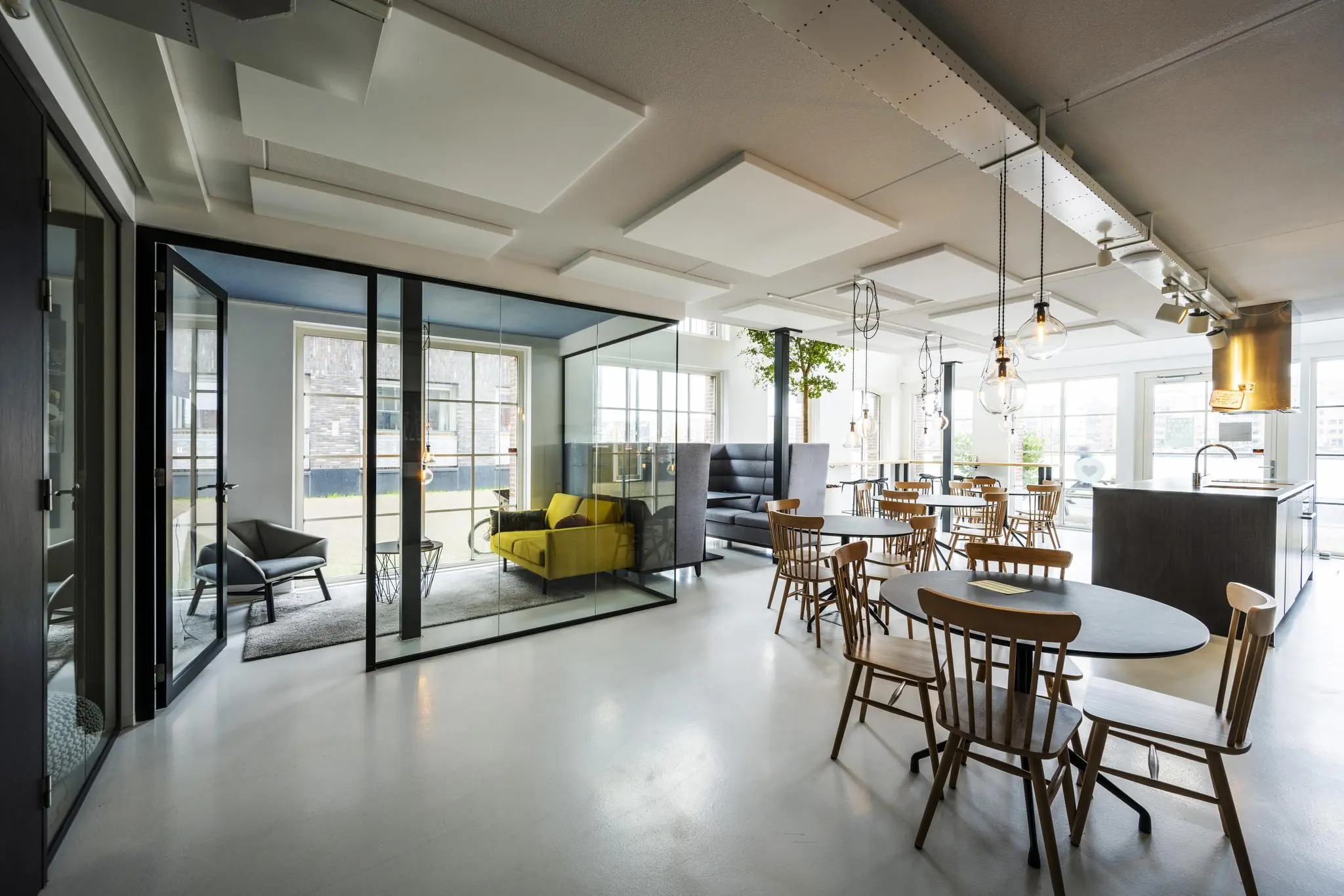 Modern ingericht kantoor aan de Oostelijke Handelskade met glazen vergaderruimte, open zithoek en eetgedeelte met houten tafels en stoelen.