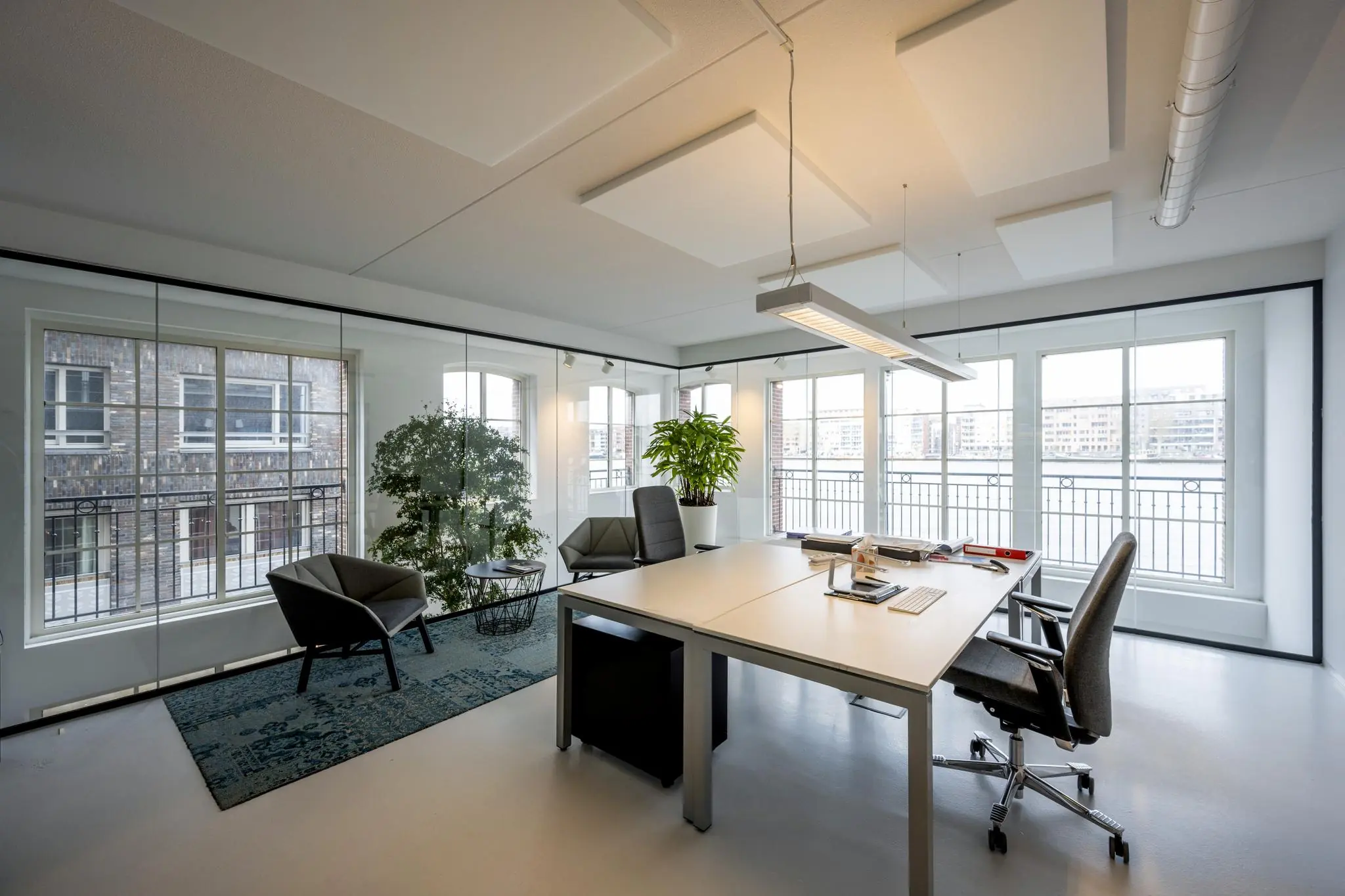 Modern kantoor aan de Oostelijke Handelskade met glazen wanden, bureaus, planten en uitzicht op het water.