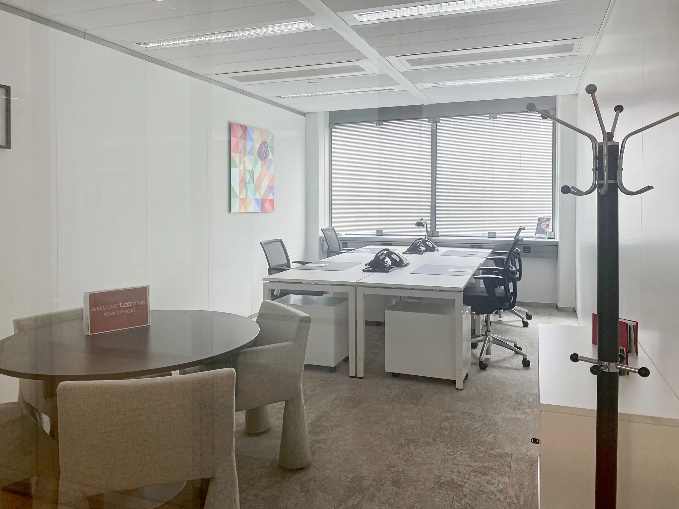 Een moderne kantoorruimte met bureaus, stoelen, een ronde tafel, kunst aan de muur en een kapstok.