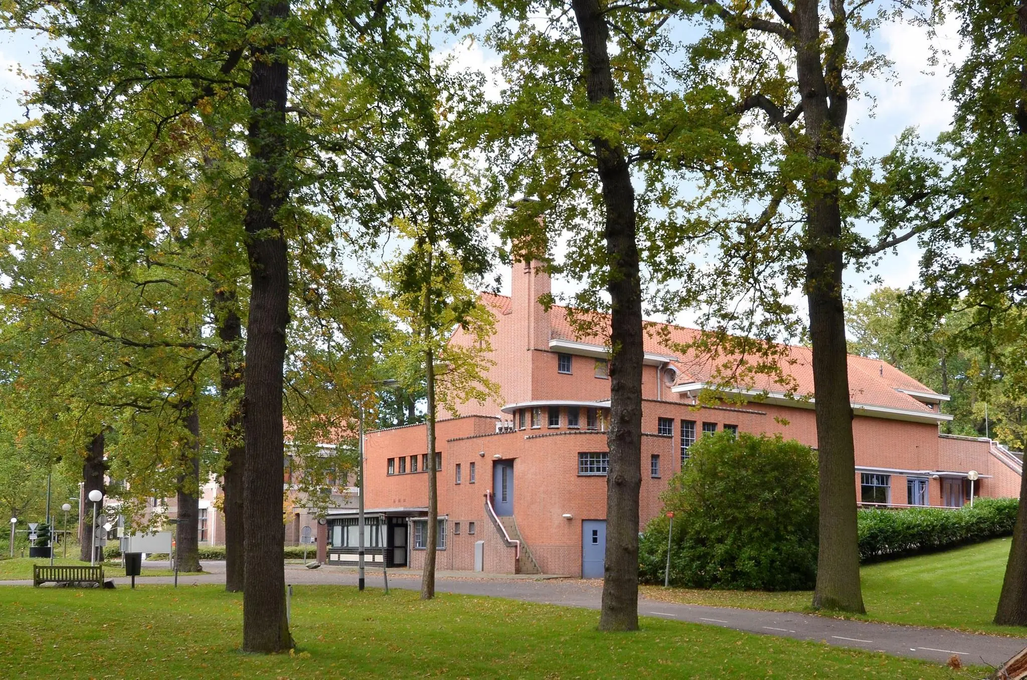 Bakstenen gebouw aan de Endegeesterstraatweg, omringd door groene bomen en een grasveld.