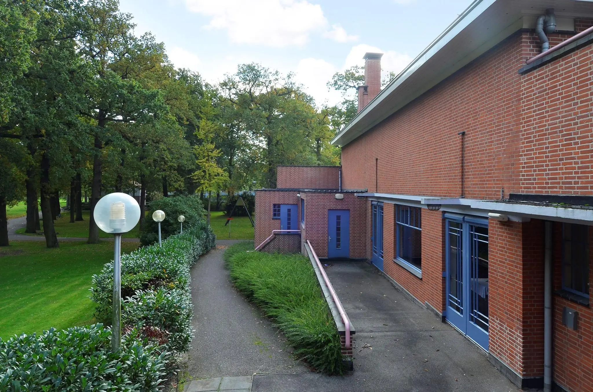 Pad met lantaarns langs een rood bakstenen gebouw aan de Endegeesterstraatweg, omgeven door groen en bomen.