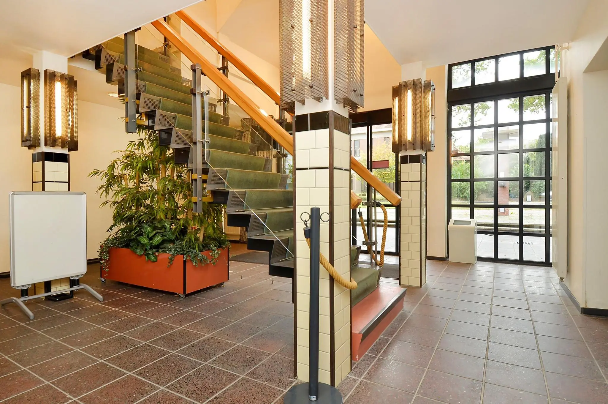 Entreehal van een gebouw aan de Endegeesterstraatweg met groene trap, grote ramen en plantenbak.
