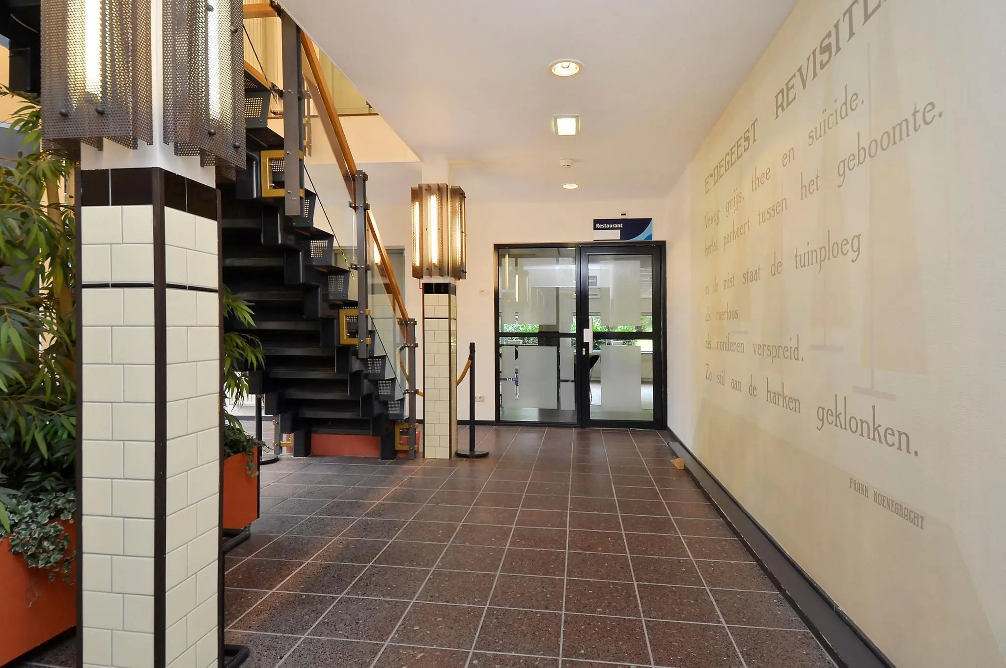 Ingangshal van een gebouw aan de Endegeesterstraatweg met een trap, planten, wandverlichting en een muur met poëtische tekst.