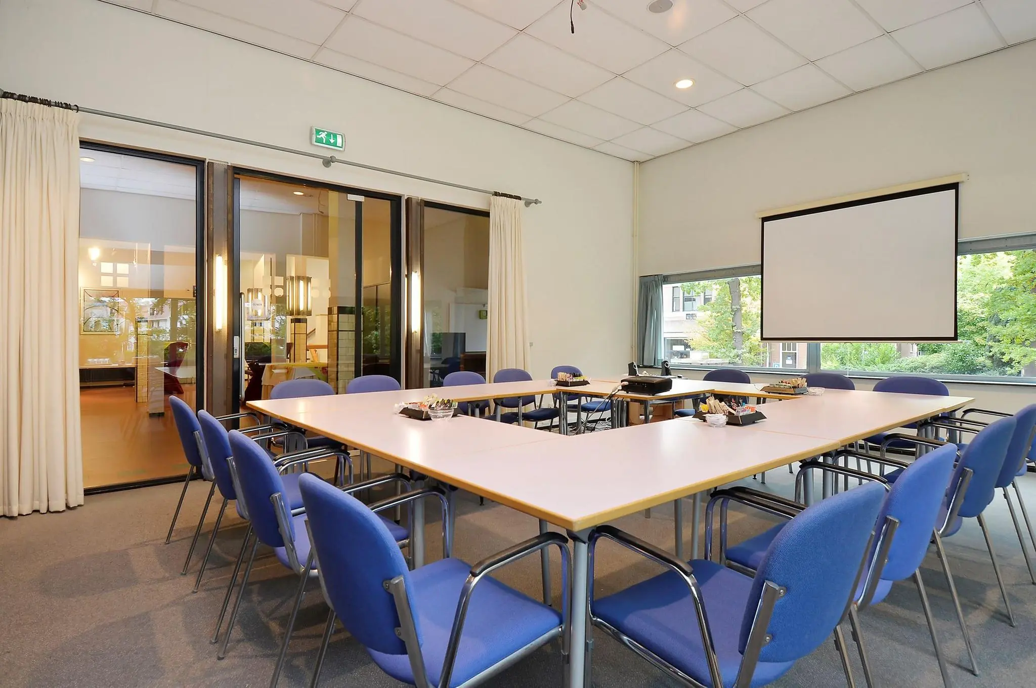 Vergaderruimte aan de Endegeesterstraatweg met een U-opstelling van tafels, blauwe stoelen en een projectiescherm.