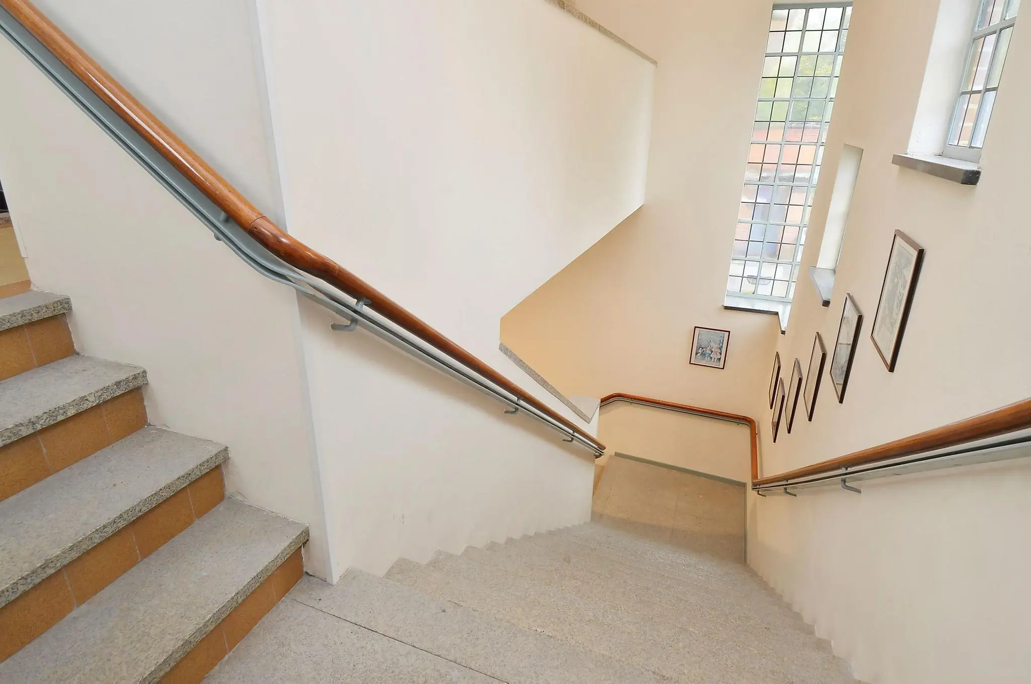 Trap met houten leuningen in een trappenhuis aan de Endegeesterstraatweg, met grote ramen en ingelijste schilderijen aan de muur.