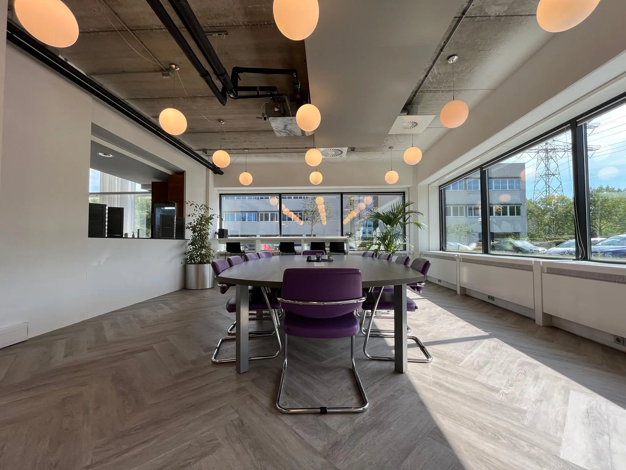 Moderne vergaderruimte aan de Savannahweg met paarse stoelen, grote ramen en sfeervolle plafondverlichting.