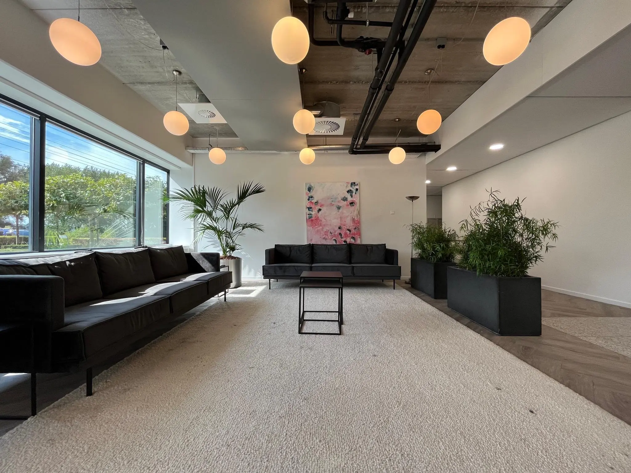 Moderne wachtruimte aan de Savannahweg met zwarte banken, hanglampen, planten en een abstract kunstwerk aan de muur.