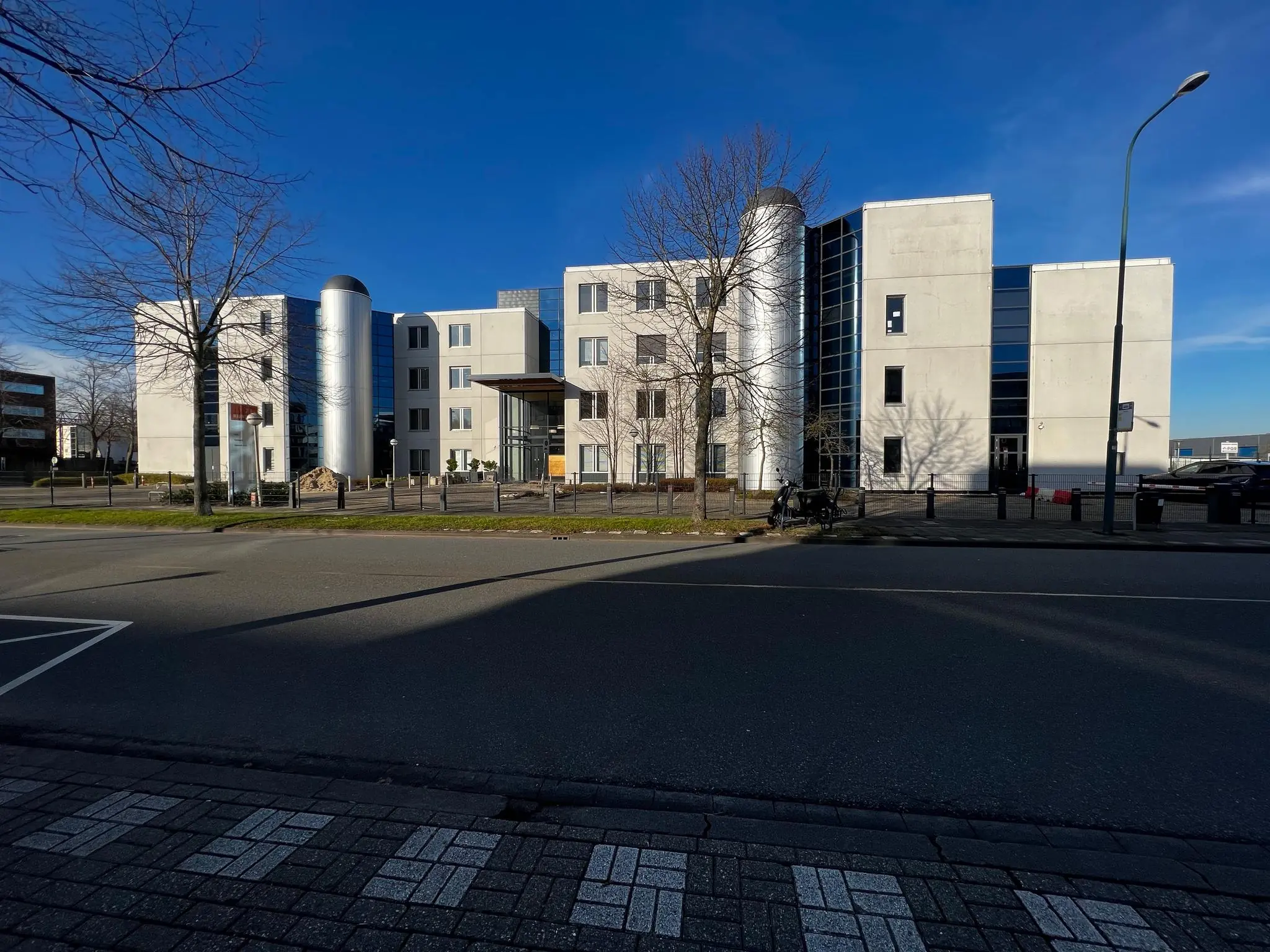 Modern kantoorgebouw aan de Rijnzathe met zilverkleurige ronde gevelaccenten en grote ramen, gezien vanaf de overkant van de straat.