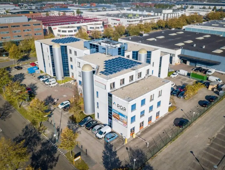 Luchtfoto van het kantoorgebouw van PQR aan de Rijnzathe, met zonnepanelen op het dak en omliggende parkeerplaatsen.
