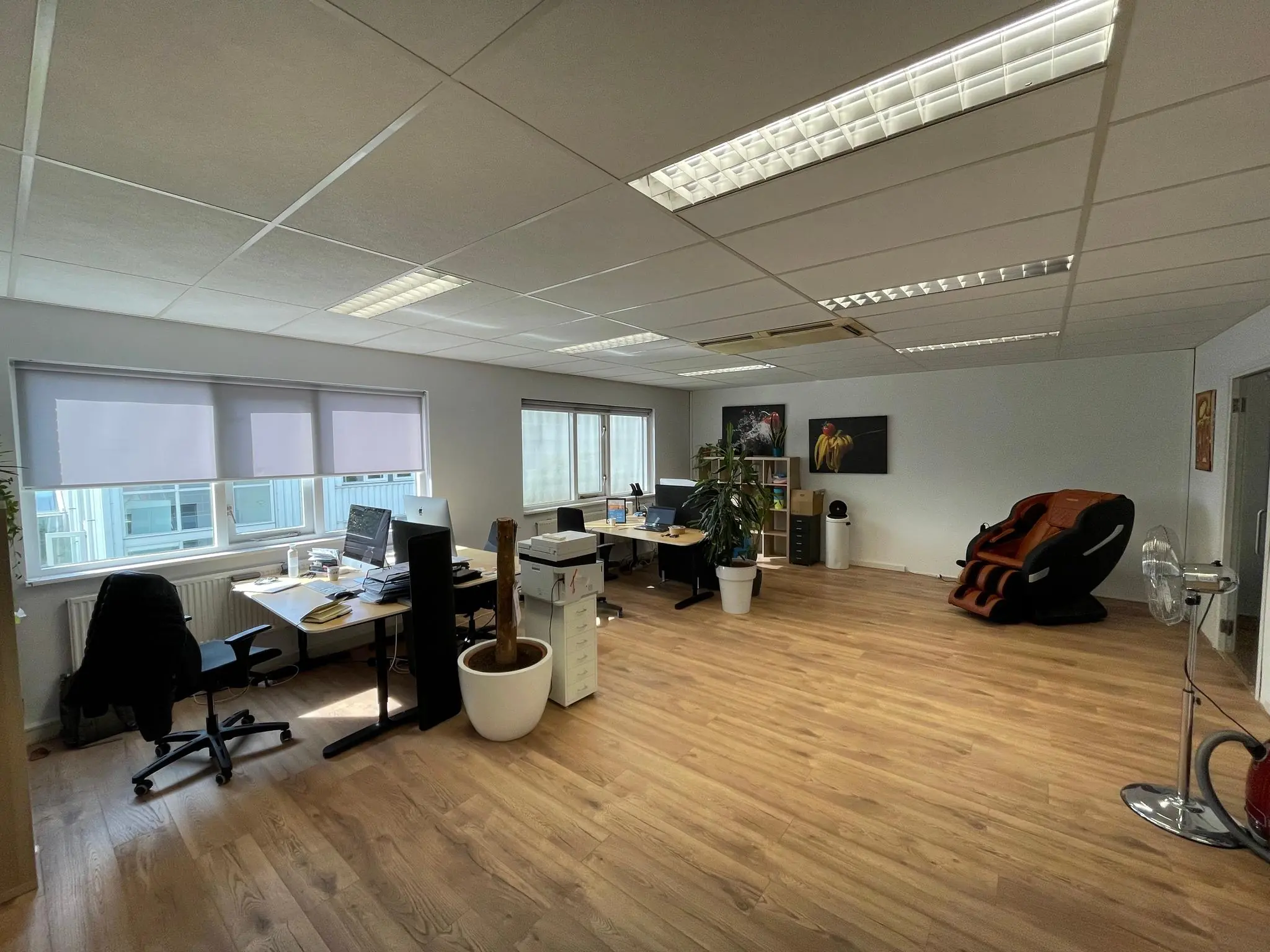 Modern kantoor aan de Computerweg met bureaus, computers, een massagestoel en houten vloer.
