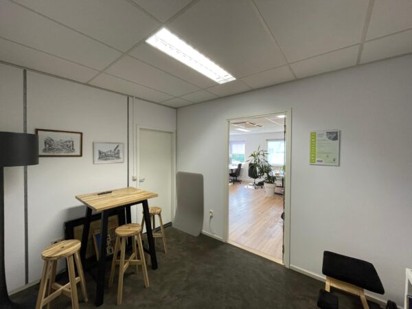 Kleine wachtruimte met hoge tafel, krukken en uitzicht op een modern kantoor op Computerweg.