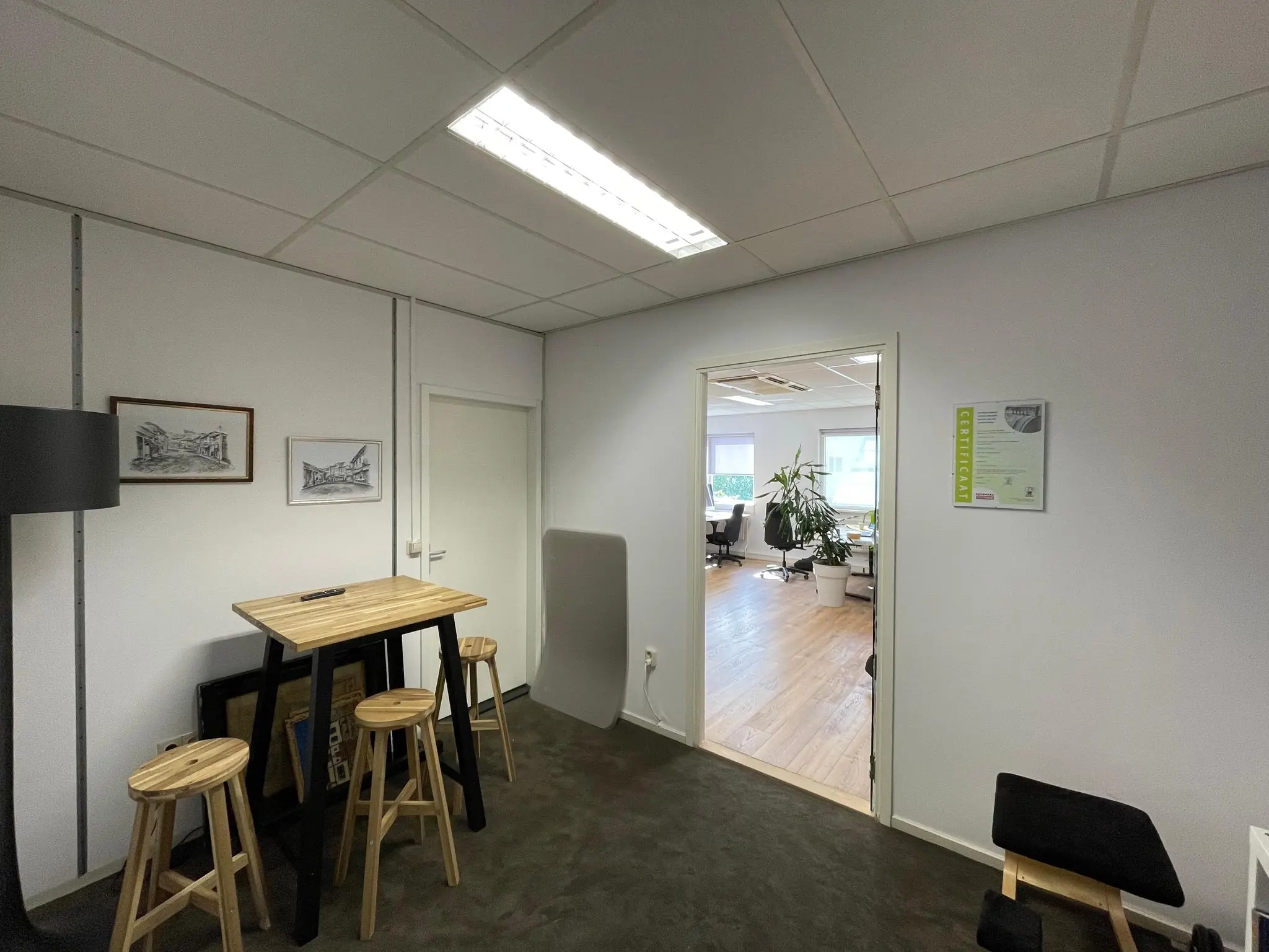 Kleine wachtruimte met hoge tafel, krukken en uitzicht op een modern kantoor op Computerweg.