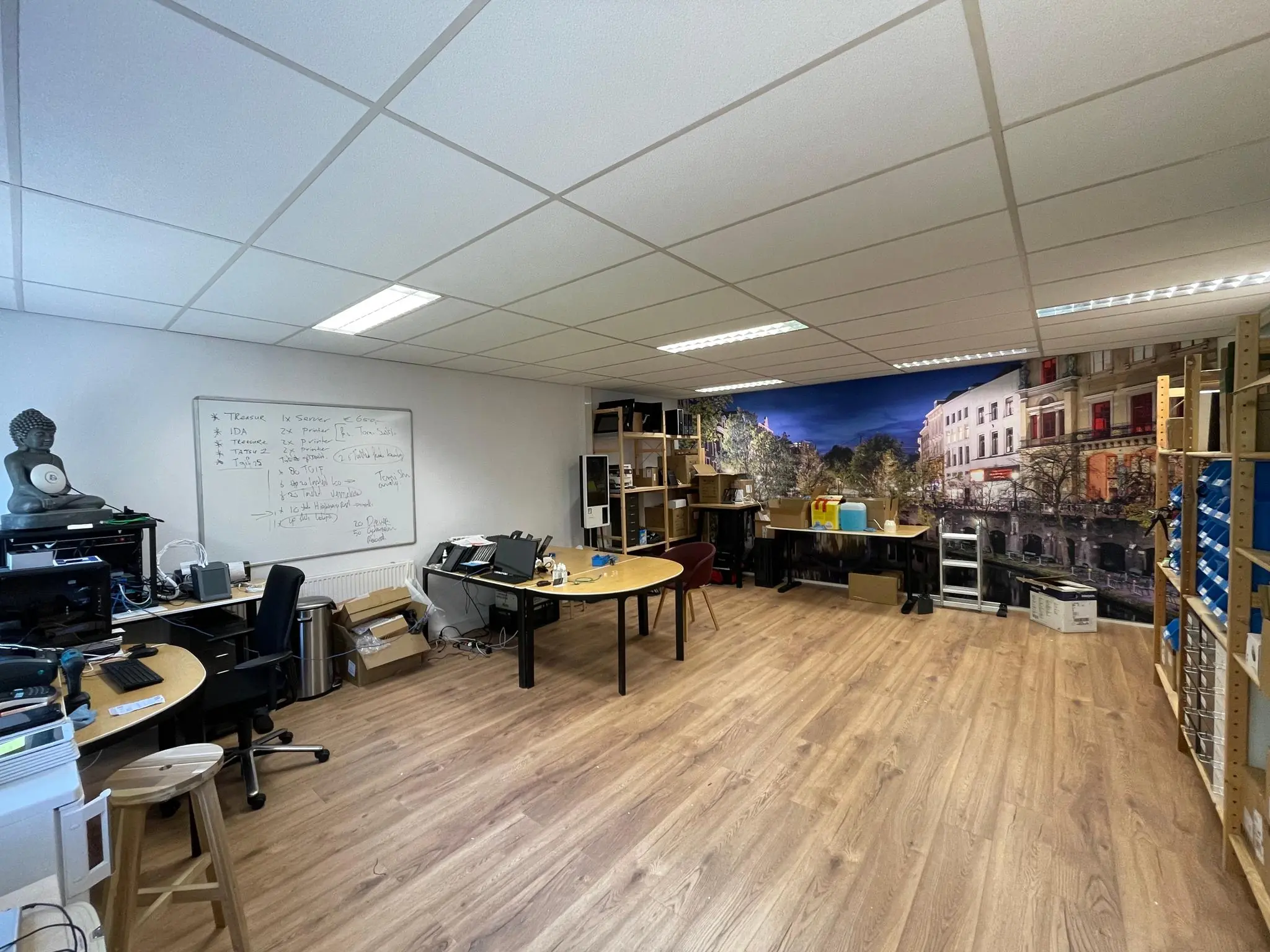 Kantoorruimte aan de Computerweg met werktafels, opslagrekken en een muurdecoratie van een stadsgezicht.