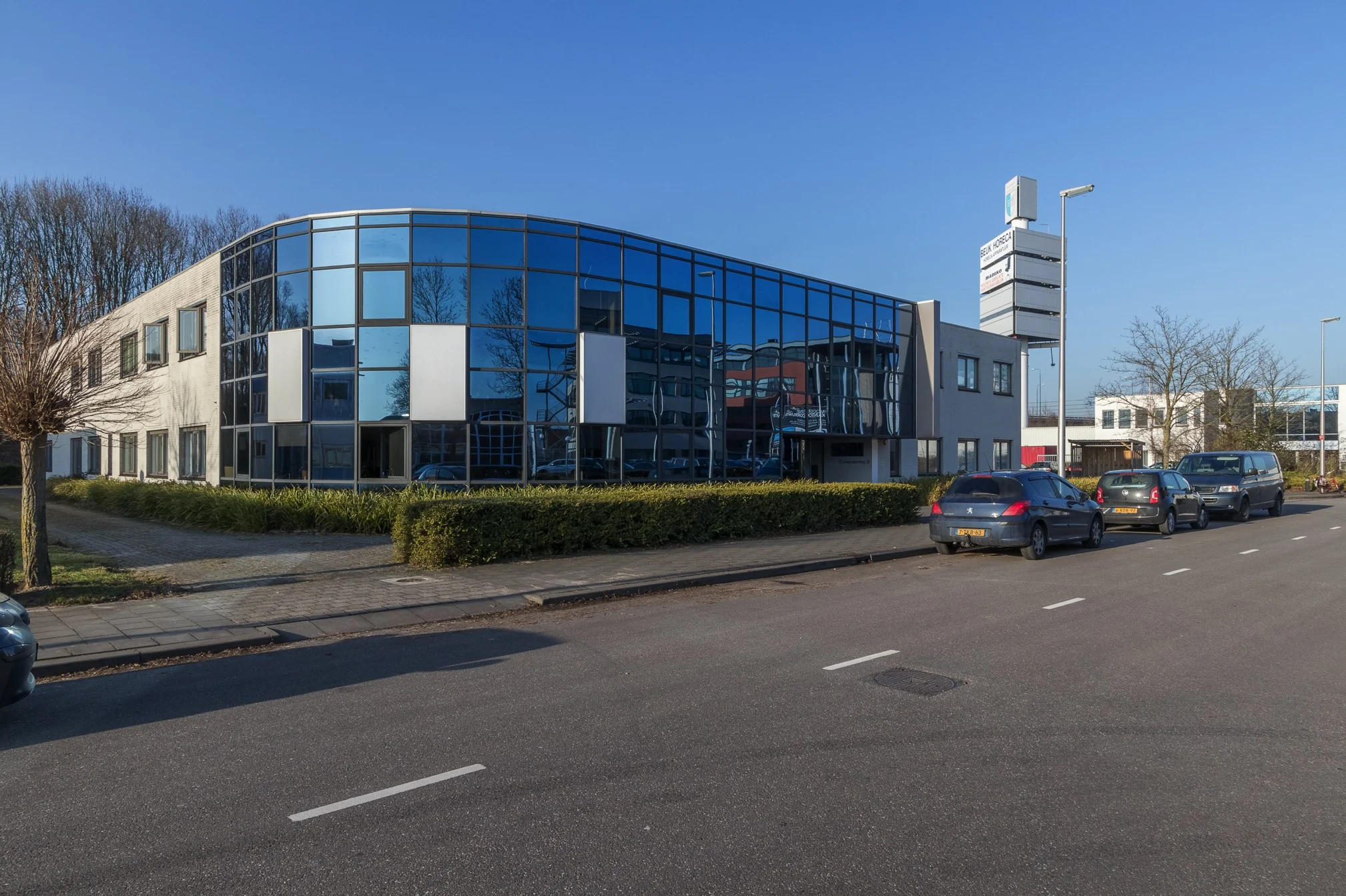 Modern kantoorgebouw met spiegelende gevel aan de Computerweg, met geparkeerde auto's langs de straat.