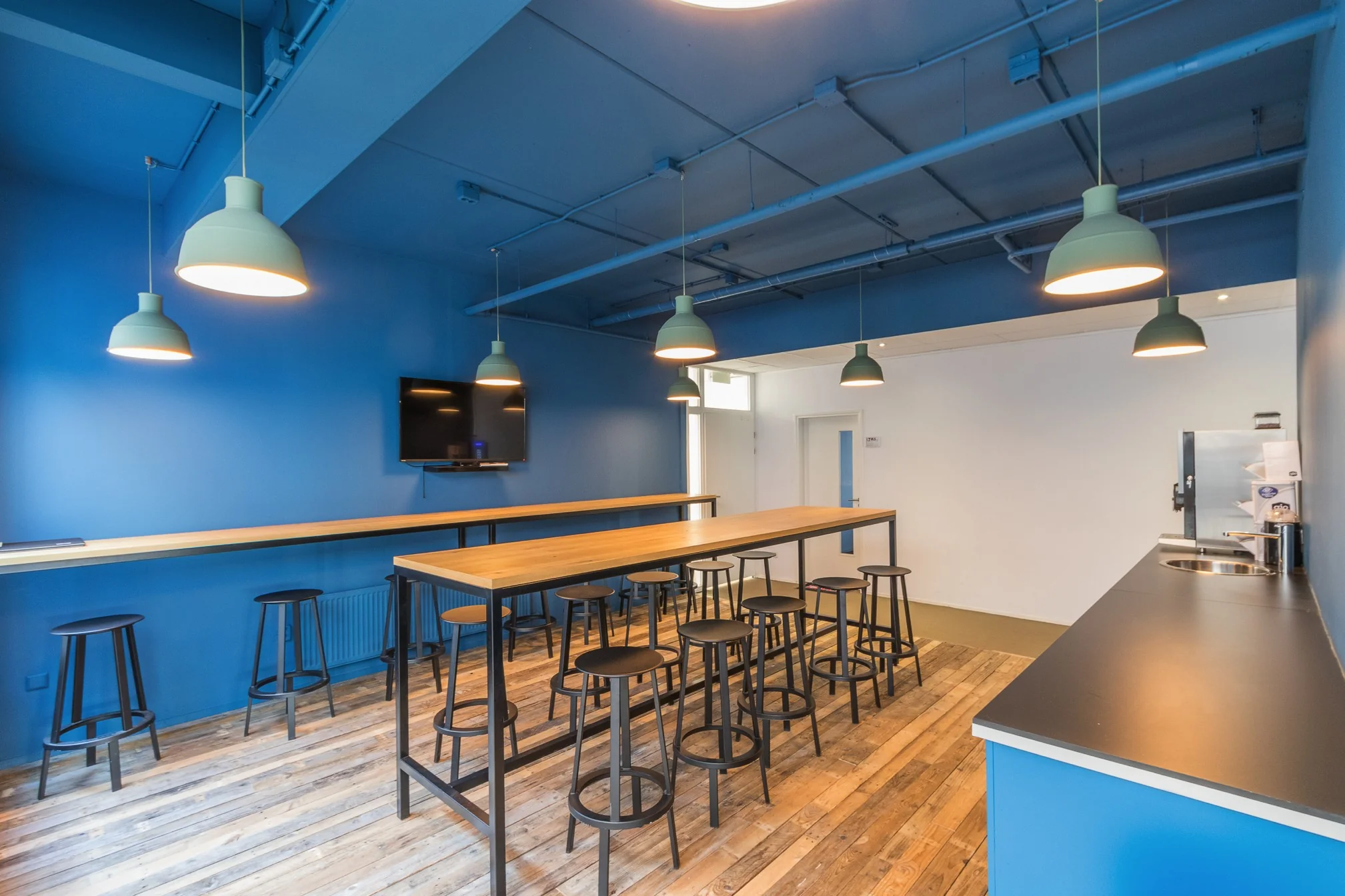 Moderne kantineruimte aan de Computerweg met houten vloer, blauwe wanden, hoge tafels en barkrukken.