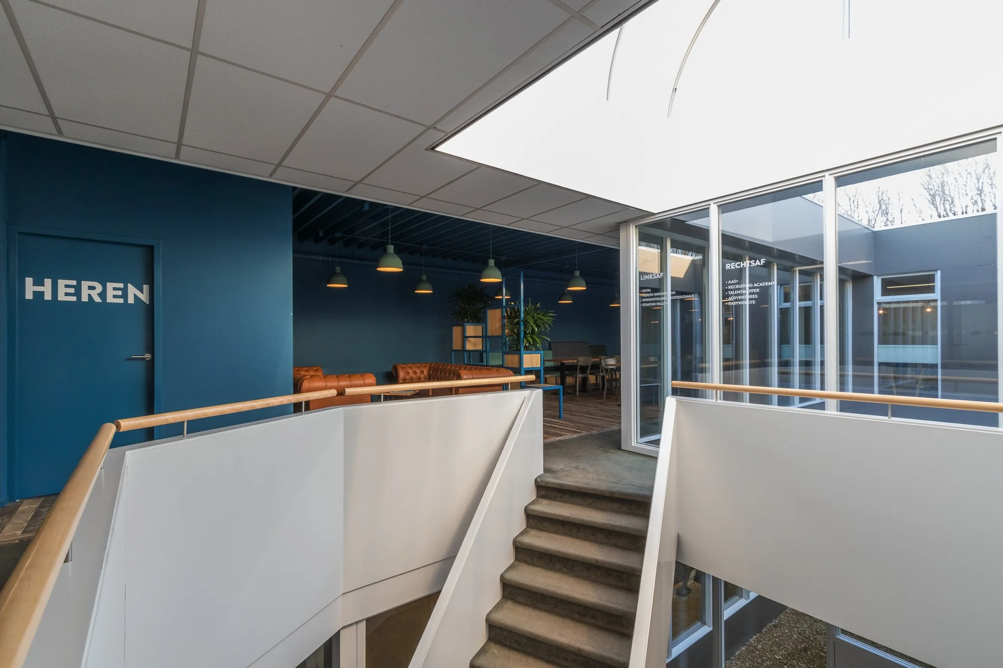 Trapopgang met witte balustrade in een modern kantoorgebouw aan de Computerweg, met zicht op zitruimte en blauwe muren.