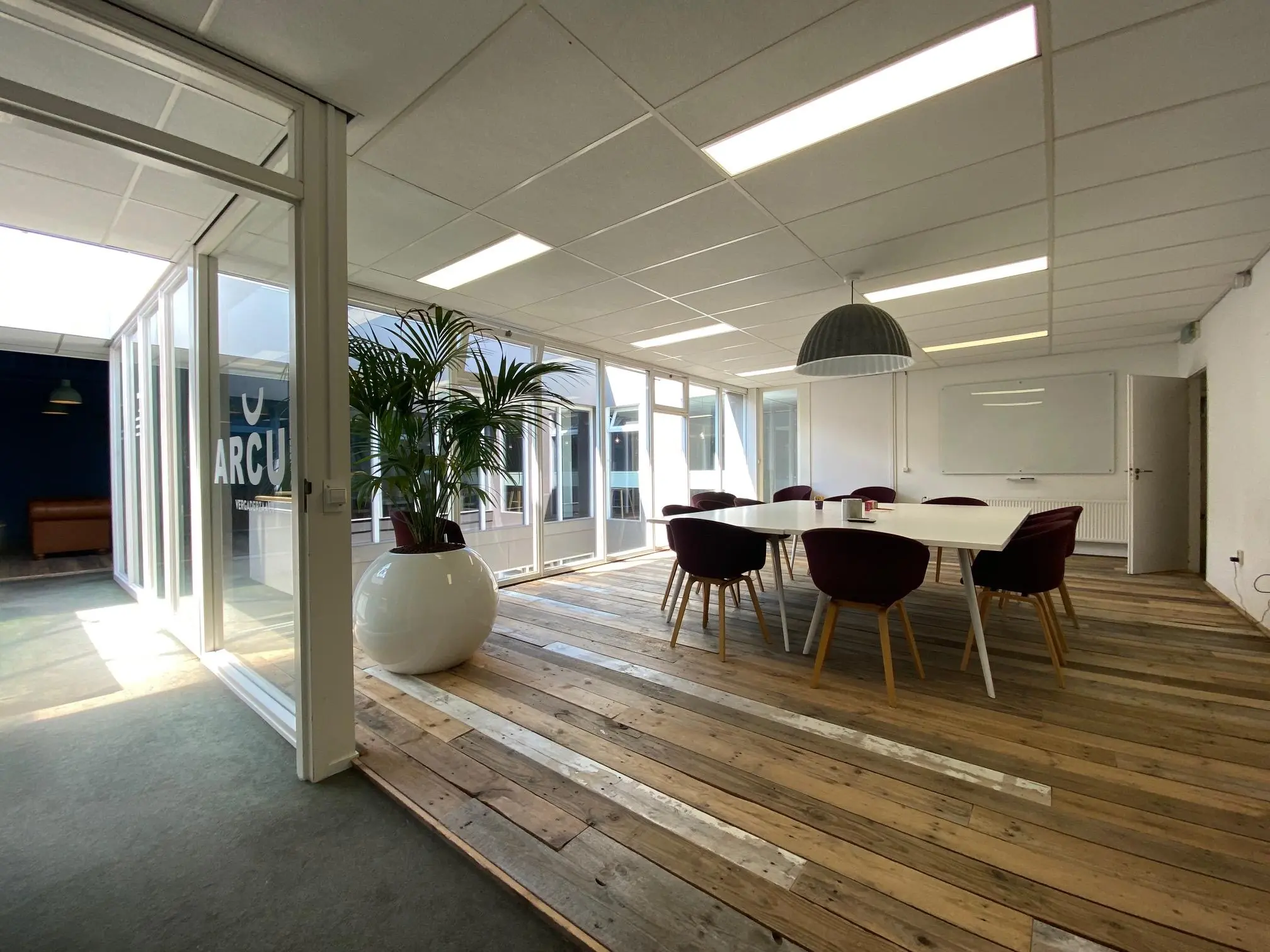 Vergaderruimte met een grote witte tafel, omringd door paarse stoelen en omgeven door glazen wanden bij Computerweg.