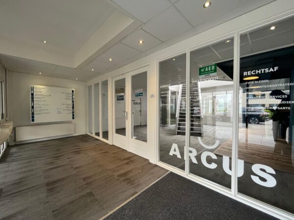 Ingang van kantoorgebouw Arcus aan de Computerweg met glazen deuren en bedrijfsnamen op de ruiten.