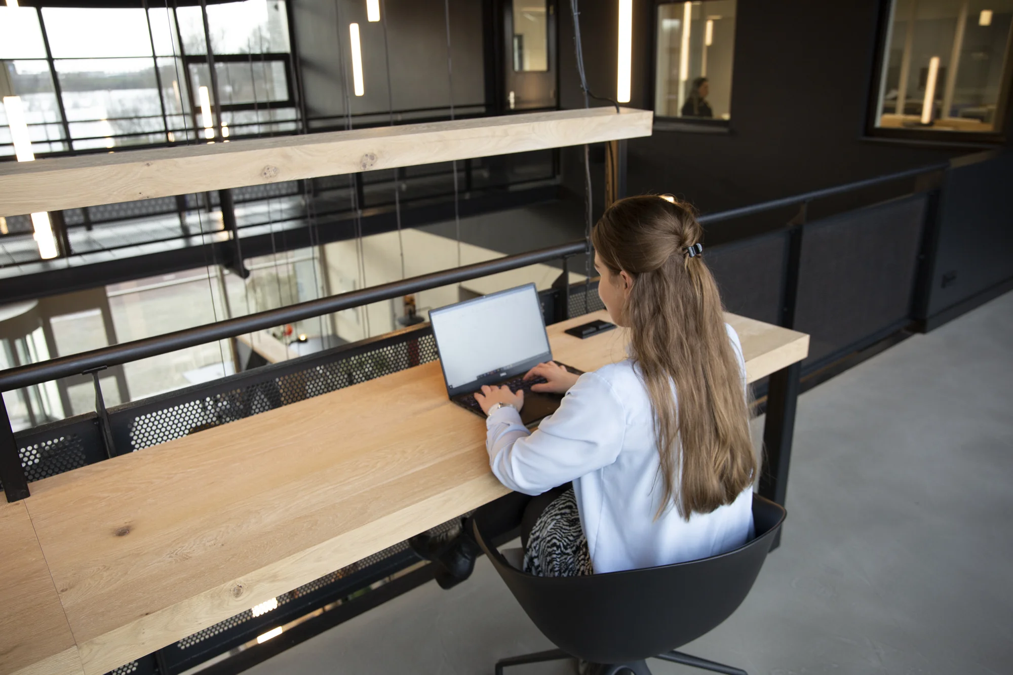 Vrouw werkt op een laptop aan een houten bureau in een modern kantoorpand aan de Atoomweg.
