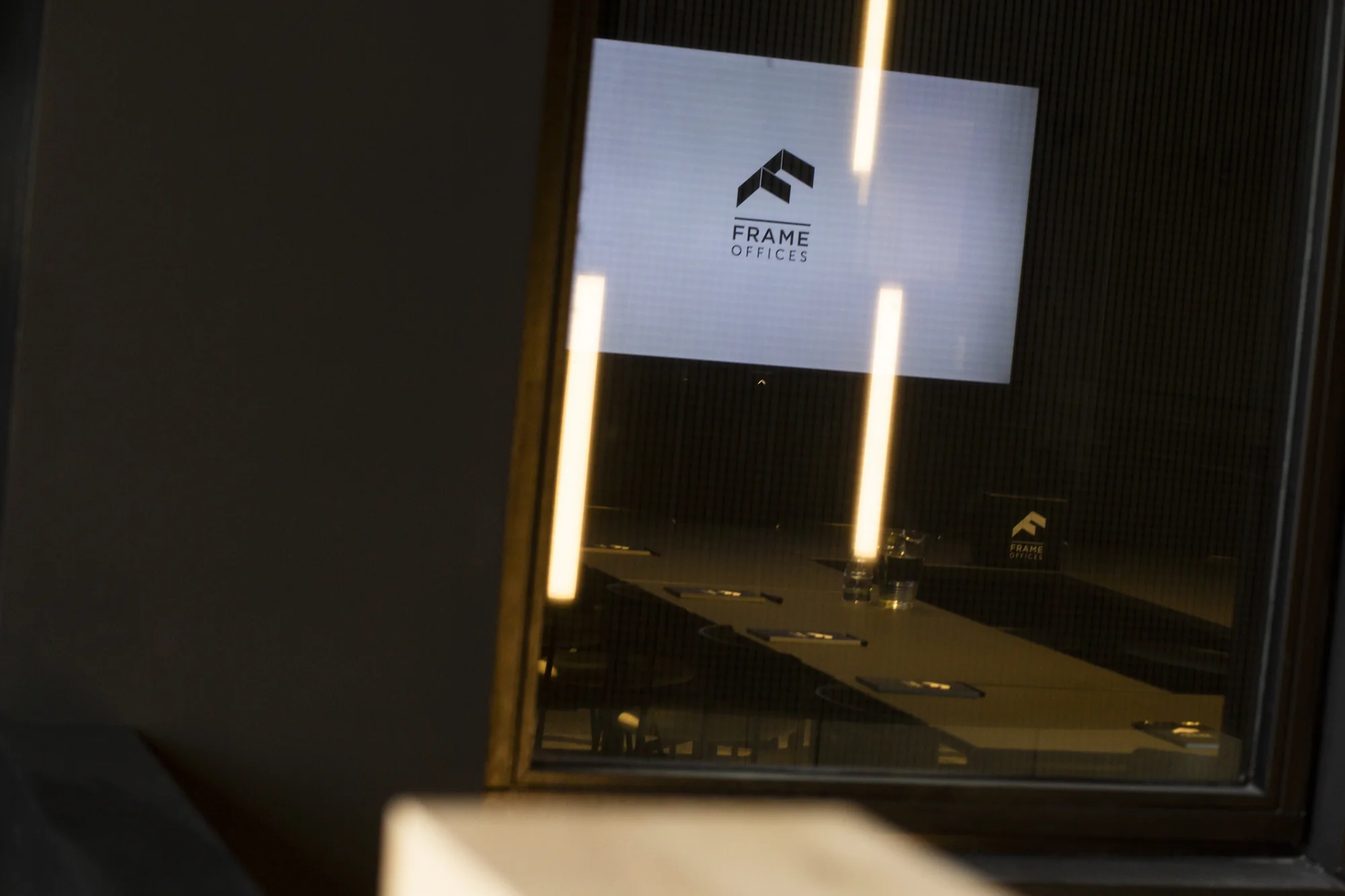 Vergaderruimte bij Frame Offices aan de Atoomweg, gezien door een glazen raam met reflectie van verlichting.