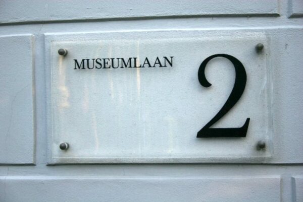 Huisnummerbord met het adres Museumlaan 2 bevestigd op een witte gevel.