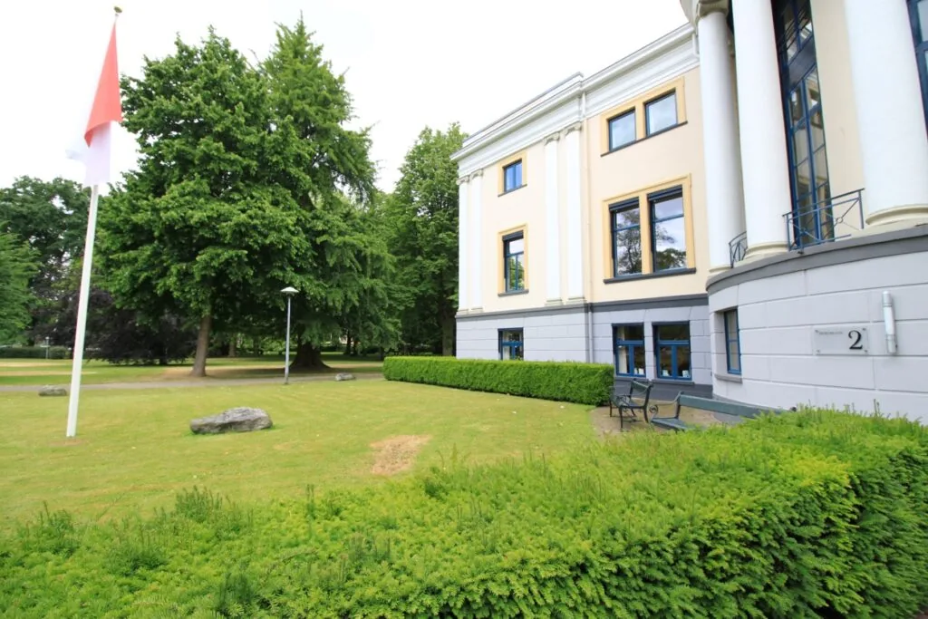 Vooraanzicht van een klassiek gebouw aan de Museumlaan met een goed onderhouden tuin en een Nederlandse vlag.