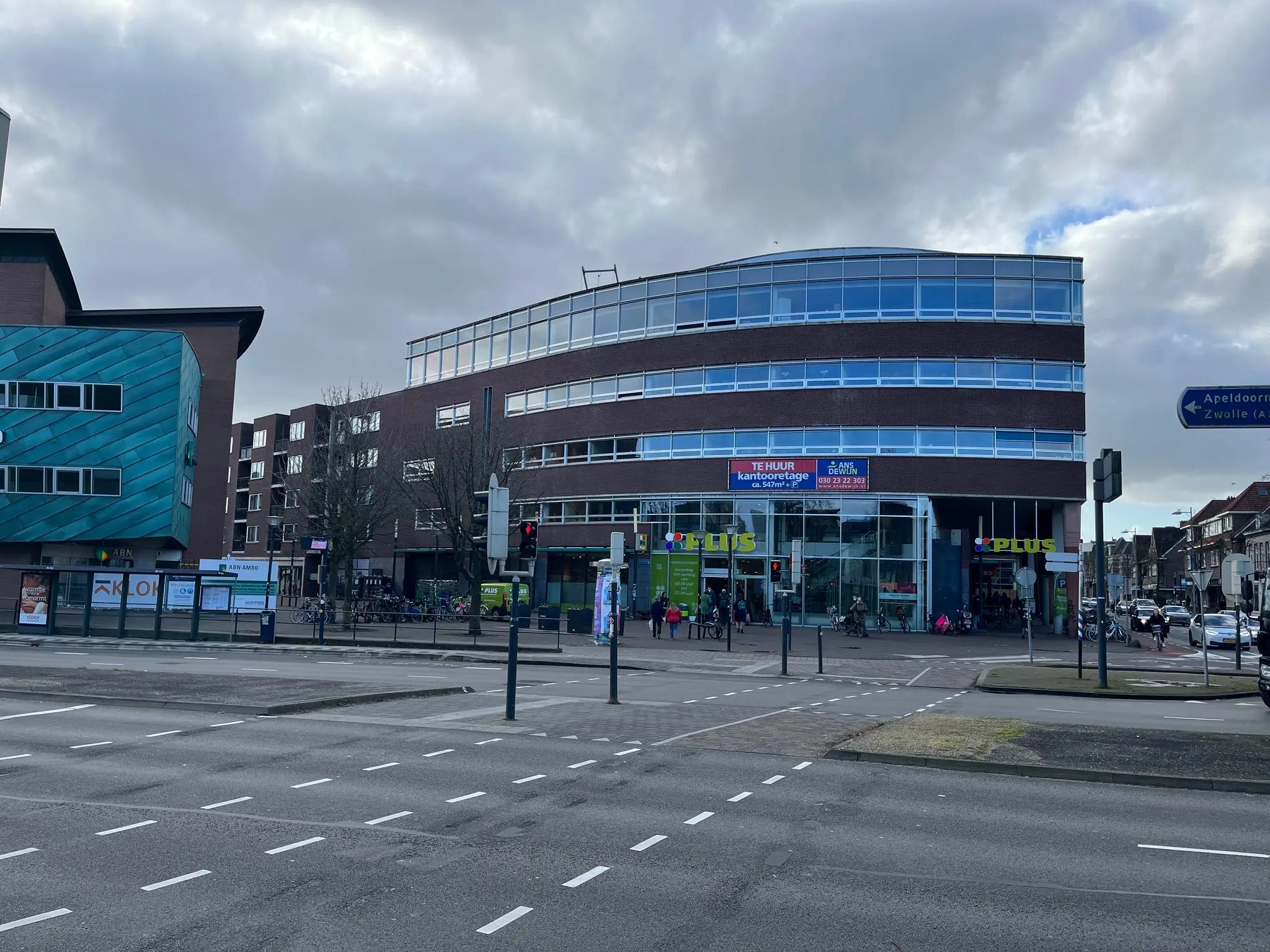 Straatbeeld van de Arnhemseweg met een PLUS supermarkt in een modern kantoorgebouw op de hoek.
