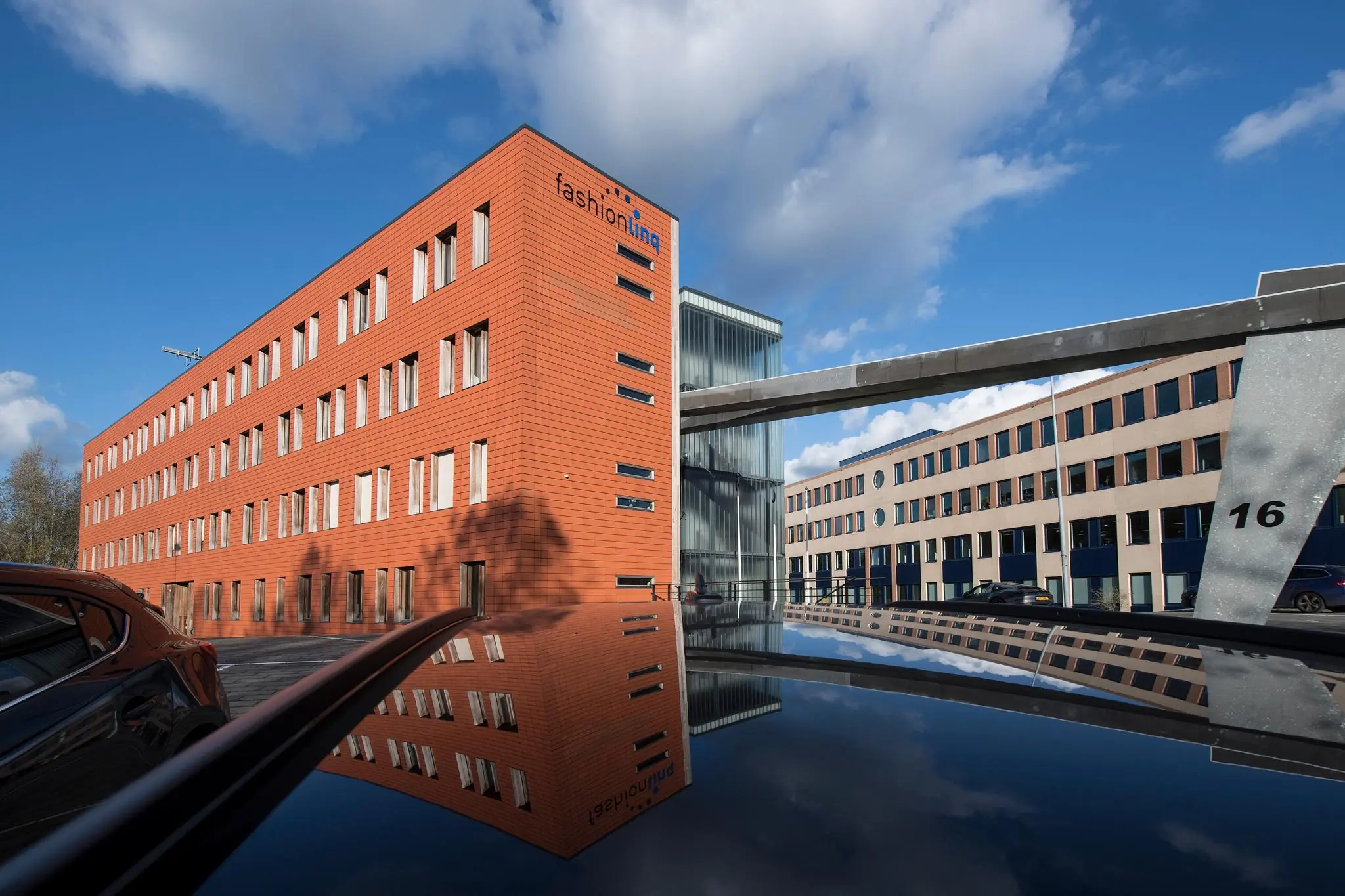 Kantoorgebouw van Fashionlinq aan de Fokkerstraat met spiegeling in autodak onder een blauwe lucht.