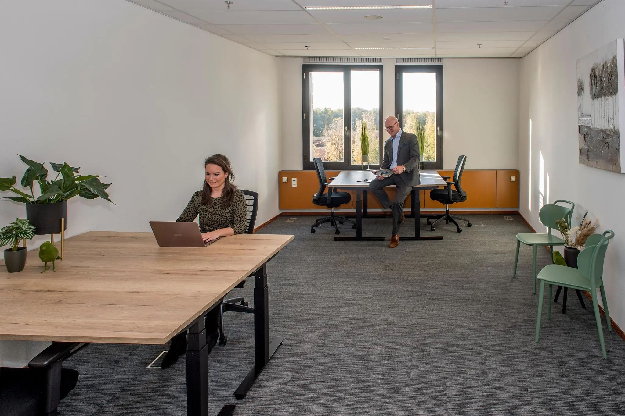 Twee mensen werken in een modern, licht kantoor aan de Fokkerstraat met bureau's, planten en grote ramen.