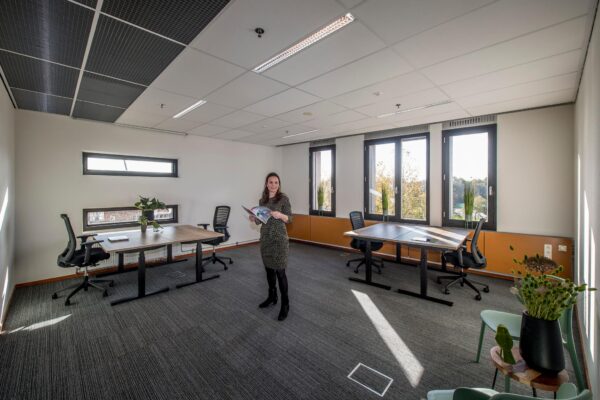 Vrouw staat met brochure in een modern, licht kantoorpand aan de Fokkerstraat met meerdere bureaus en stoelen.
