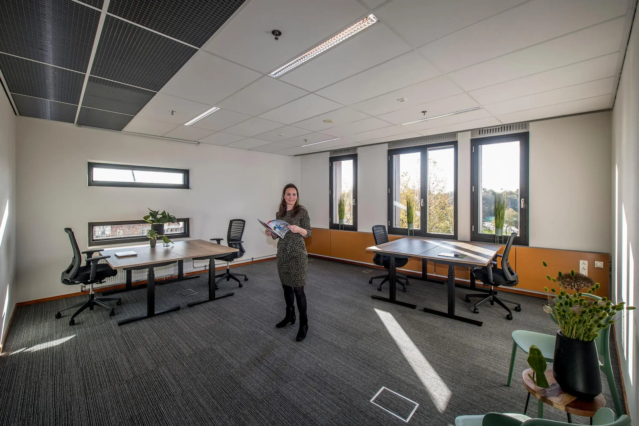Vrouw staat met brochure in een modern, licht kantoorpand aan de Fokkerstraat met meerdere bureaus en stoelen.