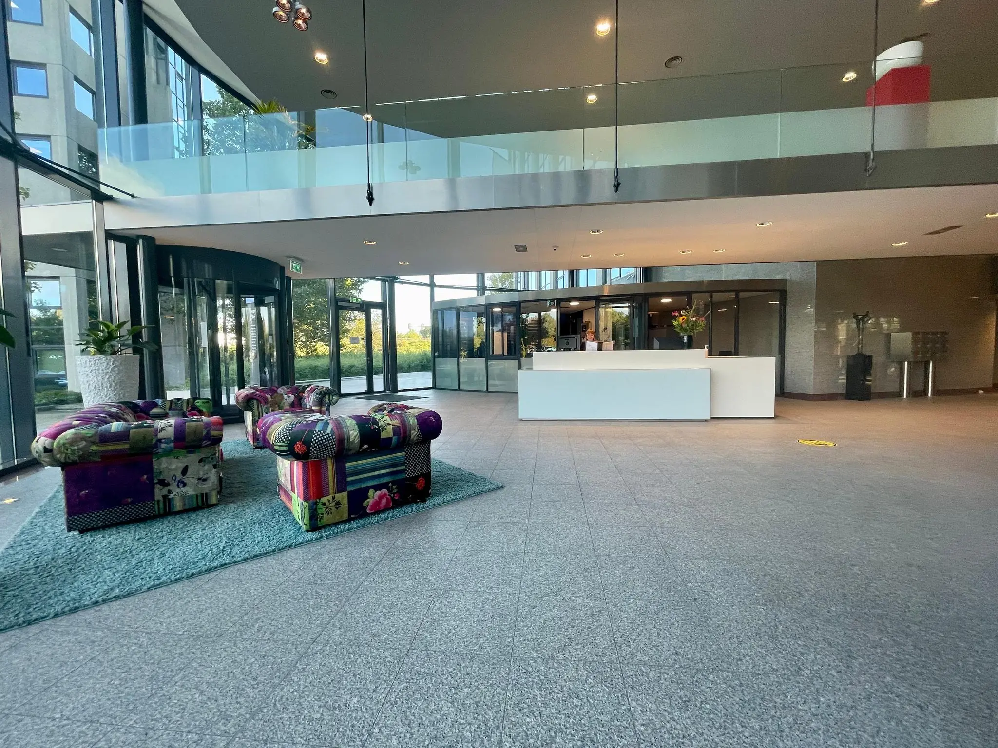 Moderne ontvangsthal van het kantoorgebouw Nevelgaarde met kleurrijke fauteuils, glazen entree en witte receptiebalie.