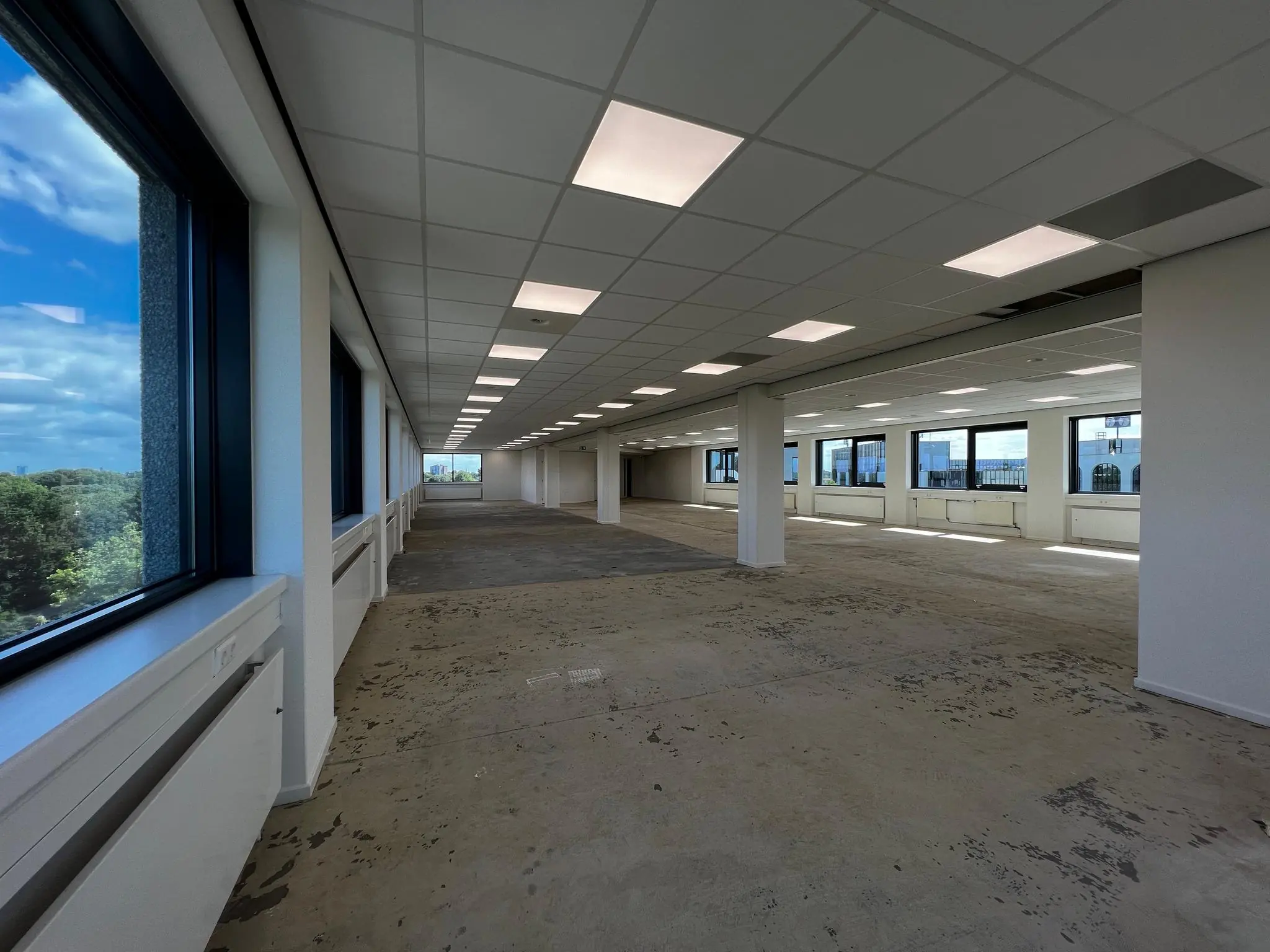 Leeg kantoorpand aan de Nevelgaarde met systeemplafond, grote ramen en onafgewerkte vloer.