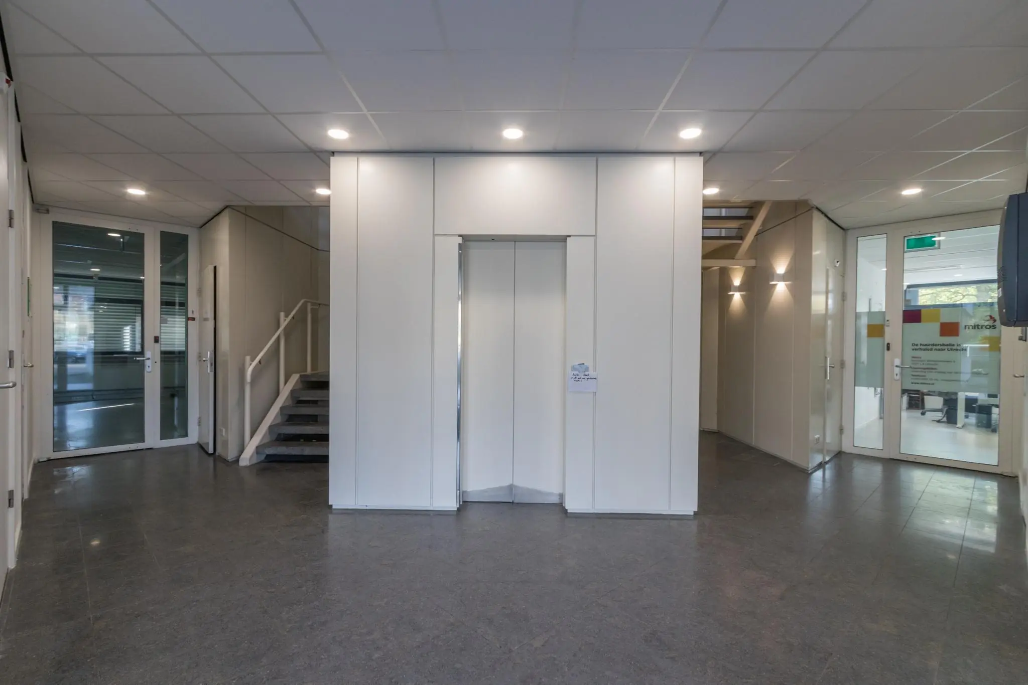 Hal met een lift in het midden, trappen aan beide zijden en glazen deuren naar kantoren aan de Vreeswijksestraatweg.
