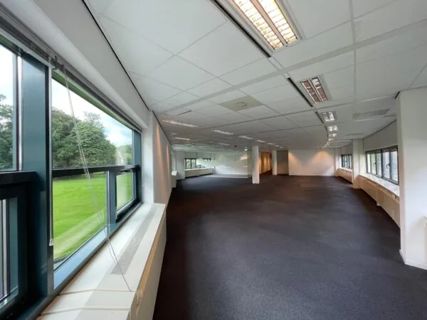 Lege kantoorruimte in kantoorgebouw Sparrenheuvel met grote ramen en uitzicht op een groen grasveld.