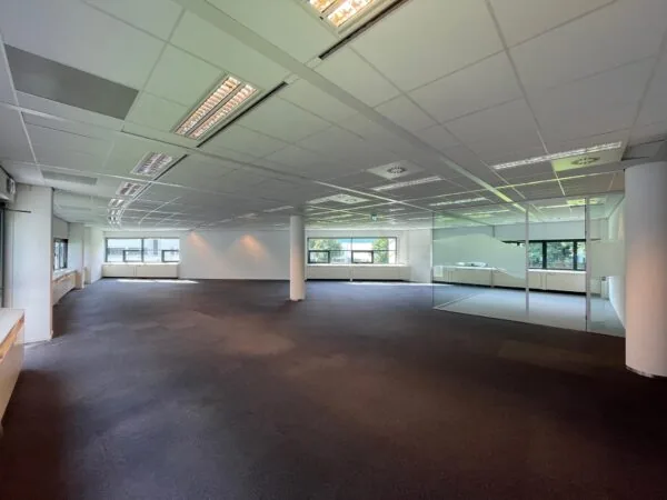 Ruime, lege kantoorruimte in Sparrenheuvel met grote ramen en een glazen vergaderruimte.