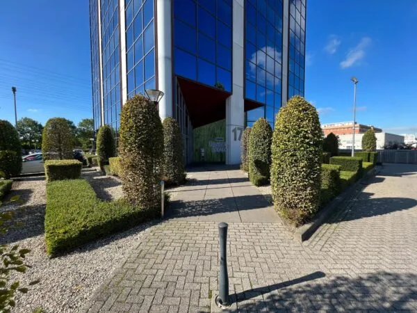 Ingang van het kantoorgebouw aan de Savannahweg 17 met strak gesnoeide buxushagen en spiegelende ramen.