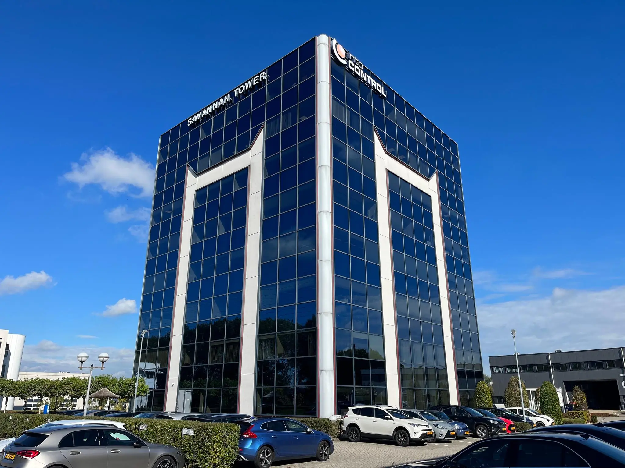 Zakelijk kantoorgebouw Savannah Tower met glazen gevel en geparkeerde auto's op de voorgrond.