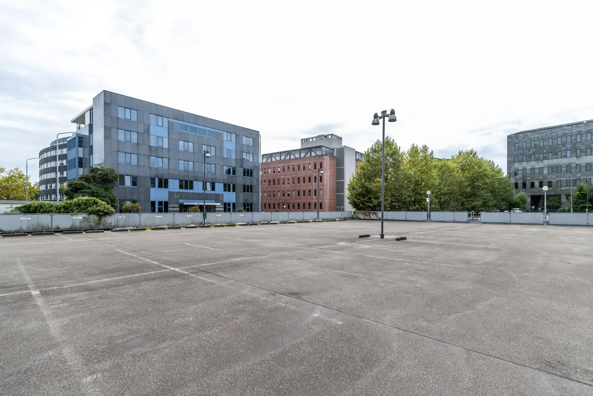 Leeg parkeerterrein aan de Pythagoraslaan met omliggende kantoorgebouwen en bomen.