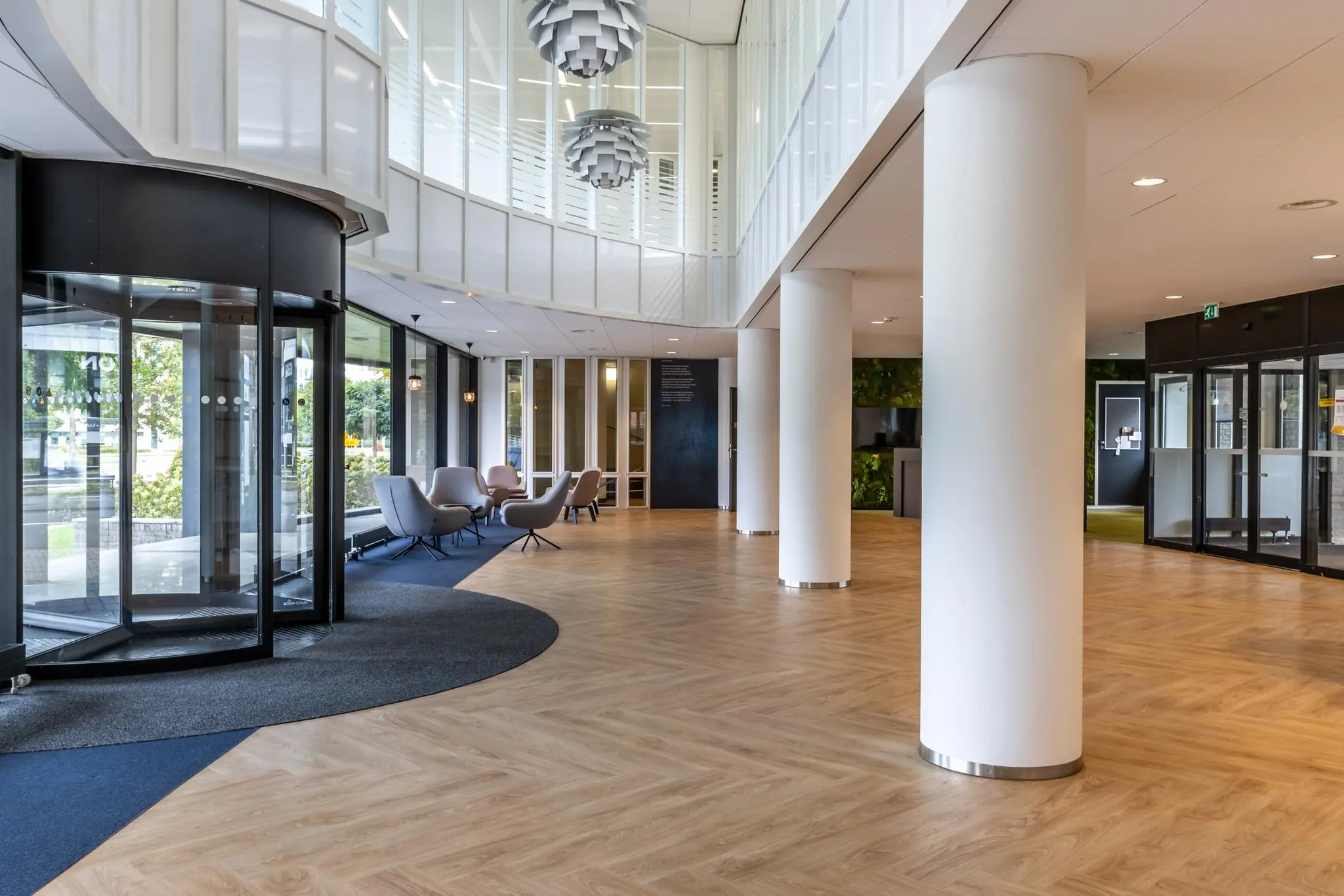 Moderne kantoorentree aan de Pythagoraslaan met zitgedeelte, houten vloer en glazen draaideur.