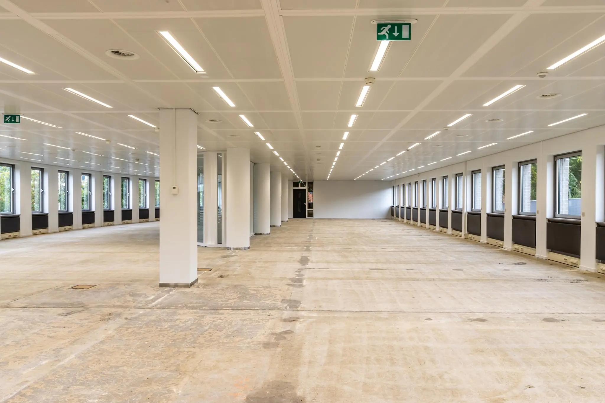 Leeg kantoorpand aan de Pythagoraslaan met witte wanden, systeemplafond en grote ramen aan beide zijden.