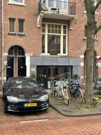 Een zwarte Tesla en meerdere fietsen geparkeerd voor een bakstenen gebouw aan de Emmastraat.