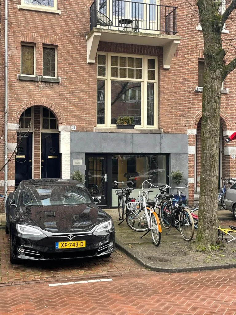 Een zwarte Tesla en meerdere fietsen geparkeerd voor een bakstenen gebouw aan de Emmastraat.